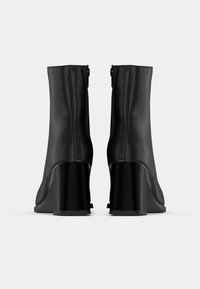 Bottes basses en cuir noir avec un talon carré haut, texture lisse, fermeture éclair latérale et design minimaliste.