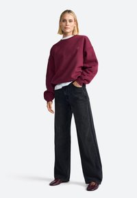 Sweatshirt bourgogne avec un col rond, coupe décontractée et poignets côtelés, associé à un jean noir à taille haute et jambes larges, et des chaussures bourgogne.