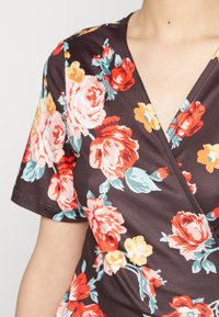 Top floral em tecido escuro com grandes rosas rosa, vermelhas e amarelas, acompanhadas de folhas verdes. Mangas curtas e design de decote em V.