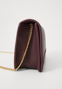 Pequena bolsa burgundy feita de couro texturizado, com uma alça de corrente dourada e um design estruturado com parte superior arredondada.