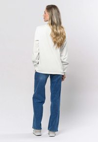 Ljusgrå sweatshirt med långa ärmar, avslappnad passform, kombinerad med blå jeans och vita sneakers. Texturerat tyg med minimala detaljer.