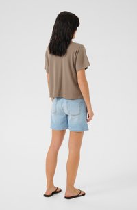 Ruskea lyhythihainen crop-top, vaaleansiniset farkkushortsit ja mustat flip-flopit. T-paidassa on lyhyet hihat ja se on rento mitoitus.