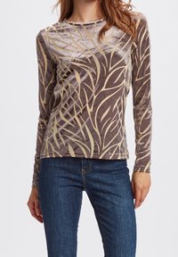 Långärmad brun topp i mjuk sammet, med ett krämfärgat växtinspirerat mönster och rund halsringning. Kombinerat med blå jeans.