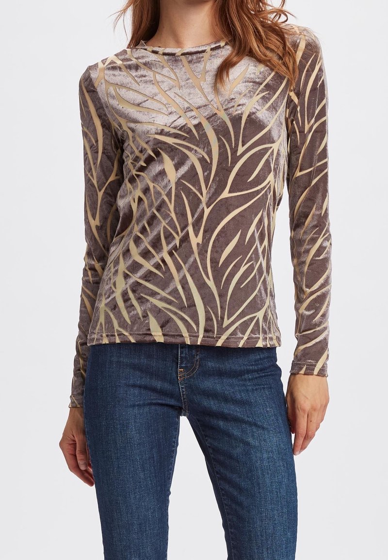 Långärmad brun topp i mjuk sammet, med ett krämfärgat växtinspirerat mönster och rund halsringning. Kombinerat med blå jeans.