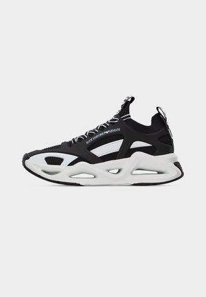 Ασπρόμαυρο sneaker EA7 Emporio Armani με παχιά σόλα, πάνω μέρος από δίχτυ, σχεδίαση με κοψίματα και κορδόνια με λογότυπο, σε απλό φόντο.