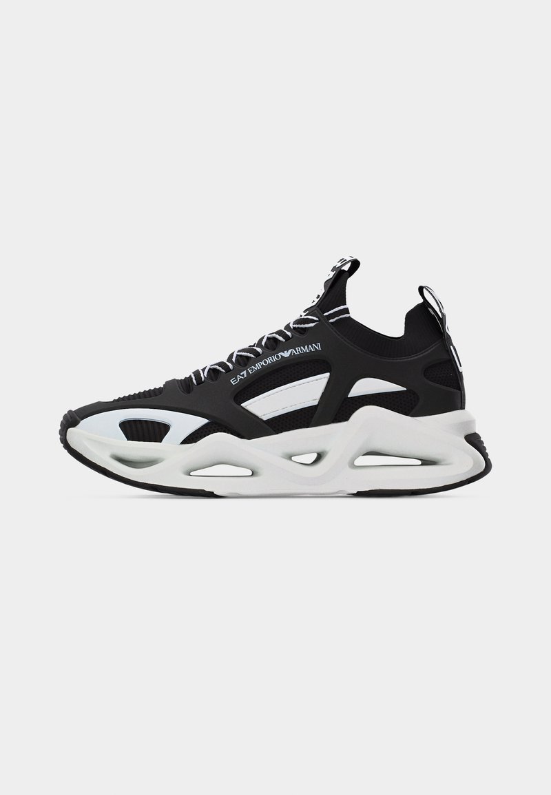 Ασπρόμαυρο sneaker EA7 Emporio Armani με παχιά σόλα, πάνω μέρος από δίχτυ, σχεδίαση με κοψίματα και κορδόνια με λογότυπο, σε απλό φόντο.