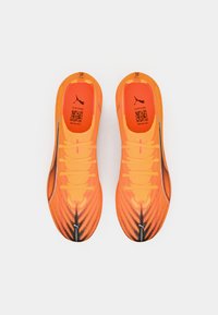 Zapatillas deportivas de un brillante color naranja con un diseño texturizado y estampado, con acentos y cordones negros. Logo de Puma visible en la parte superior.