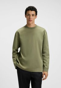 Olive green long-sleeve shirt in a soft, smooth fabric. Features a crew neckline, relaxed fit, and subtle stitching details on sleeves.