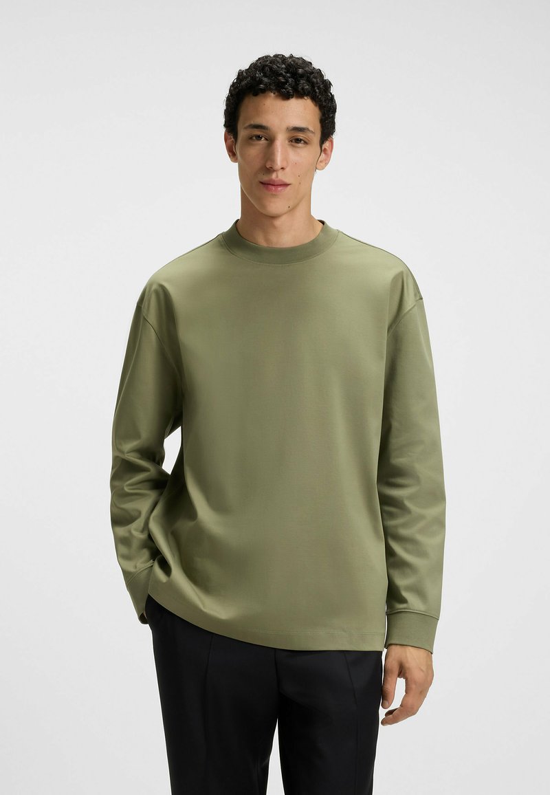 Olive green long-sleeve shirt in a soft, smooth fabric. Features a crew neckline, relaxed fit, and subtle stitching details on sleeves.