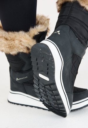 Botte d'hiver noire avec une bordure en fausse fourrure, texture matelassée, semelle intermédiaire blanche et semelle extérieure en caoutchouc à motifs pour une adhérence optimale. Logo visible sur le côté.