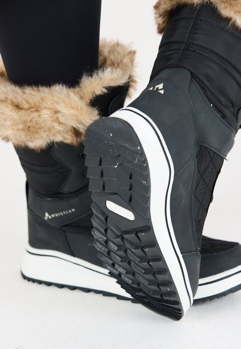 Svart vinterkänga med ett fuskpälskant, quiltad textur, vit mellansula och mönstrad gummisula för grepp. Logotyp synlig på sidan.