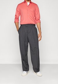 Coral long-sleeve button-up shirt paired with gray pinstripe high-waisted trousers and white sneakers featuring black stripes.