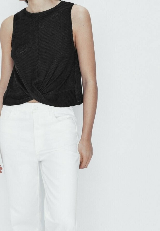 Haut noir sans manches avec un design frontal torsadé ; associé à un jean blanc taille haute. Le haut a une texture côtelée.