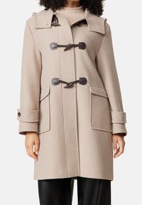 Manteau duffle beige en mélange de laine, présentant des fermetures à brandebourg, deux poches avant et un col repliable. Texture douce et coupe décontractée.