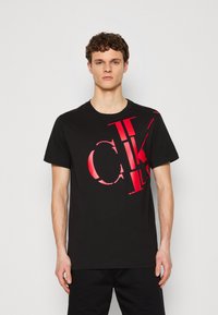 T-shirt en coton noir avec un grand logo graphique rouge. Col rond et manches courtes, avec une coupe décontractée.