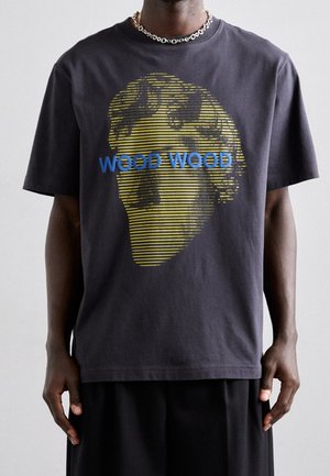 Sort t-shirt med klassisk bøstegrafik med gule striber og blå tekst "WOOD WOOD", båret af en person med mørk hud og sølvkæde.