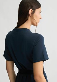 Vestito corto blu navy a maniche corte con corpetto attillato e cintura in vita, caratterizzato da una texture liscia e un design minimalista.