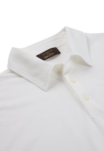 Polo à col blanc avec trois boutons et une étiquette noire visible indiquant "SLOWEAR 24 MON Icecotton" à l'intérieur du col.