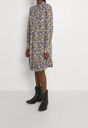 Floral dress in multicolors with long sleeves, high neckline, and ruffled hem. Worn with black cowboy boots featuring pointed toes.