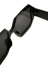 Mustad mustad geomeetrilise disainiga prillid, tumedate läätsede ja jämeda plastikraamiga. Kuju on terav, sujuvate servadega.