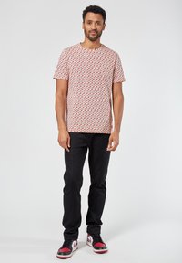 Lyhythihainen, punavalkoraidallinen t-paita, joka on valmistettu puuvillasta, yhdistettynä mustiin slim-fit-housuihin ja punaisilla yksityiskohdilla varustettuihin lenkkareihin.