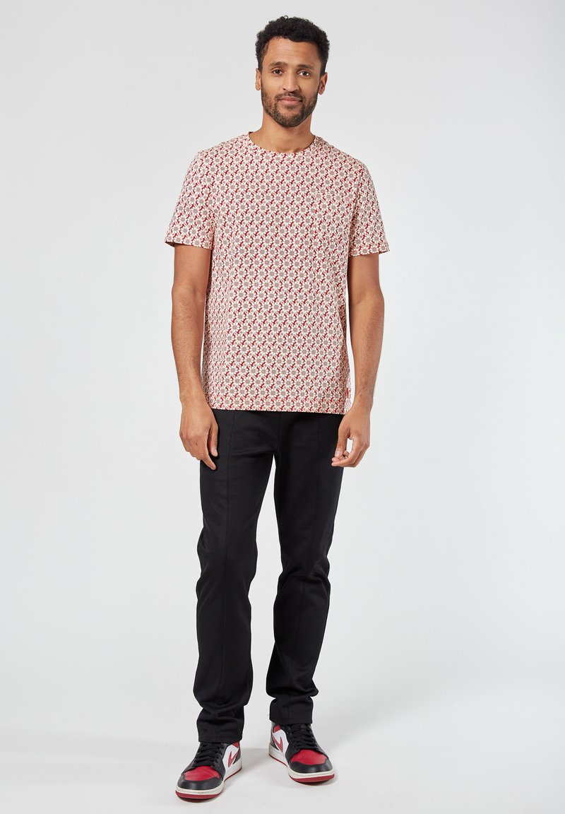 Lyhythihainen, punavalkoraidallinen t-paita, joka on valmistettu puuvillasta, yhdistettynä mustiin slim-fit-housuihin ja punaisilla yksityiskohdilla varustettuihin lenkkareihin.