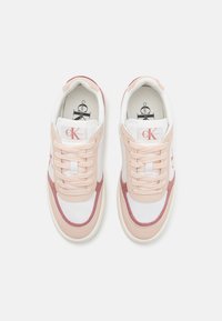 Ett par vita och rosa Calvin Klein sneakers med snörning, logotyp på tungan och sidan, sedd ovanifrån på en enkel bakgrund.