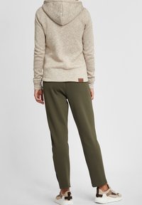 Sudadera con capucha beige de acabado texturizado, combinada con joggers verde oliva de corte entallado. Zapatos con una paleta de colores neutros y acentos en contraste.