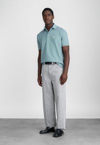 Ανοιχτό μπλε πόλο μπλούζα με γιακά, σε συνδυασμό με γκρίζες παντελόνες με φαρδιά πόδια και μαύρες δερμάτινες παπούτσια. Λείο ύφασμα με ελάχιστες λεπτομέρειες.