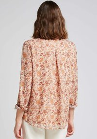 Blouse à manches longues beige clair avec imprimé floral en orange et rouge. Tissu doux avec des manches roulées et une coupe décontractée.