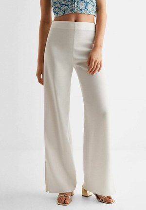 Spodnie o szerokich nogawkach w kremowym kolorze, o gładkiej fakturze i wysokim stanie. Posiadają rozcięcia przy nogawkach. Połączone z sandałami na słupku z paskami.