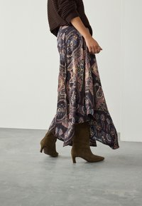 Jupe longue et fluide à imprimé paisley foncé avec des détails rose, bleu et crème. Portée avec des bottines à talons en daim vert olive. Pull marron texturé.