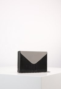 Černá kabelka s hadím vzorem s šedým lesklým klopou, která má stříbrný řetězový popruh a elegantní obálkový design. Viditelný detail texturovaného povrchu.