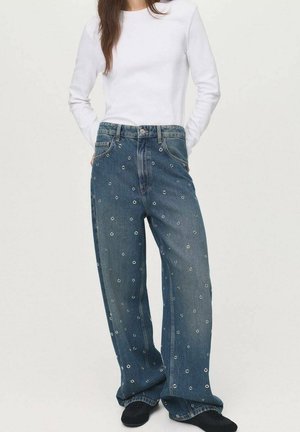 Wide-leg denim jeans with a dark wash, featuring a textured pattern of small circles and silver accents, styled with a white long-sleeve top.