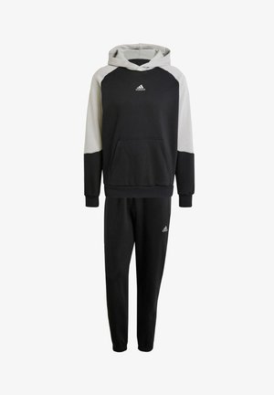 Completo sportivo in nero e grigio composto da una felpa con cappuccio e tasca anteriore e pantaloni jogger. Entrambi i capi presentano polsi elasticizzati e il logo adidas.