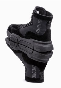 Stivaletti neri alti con un design in suede e mesh, dotati di suole in gomma spesse, lacci e un dettaglio del logo sul lato.