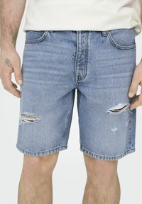 Shorts de mezclilla azul desgastados con un ajuste relajado, que presentan detalles rasgados en la parte delantera y un dobladillo recto.