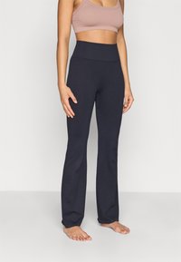 Marinblå utsvängda byxor i stretchigt tyg med mjuk textur och hög midja, kombinerade med en ljusbrun kort topp.