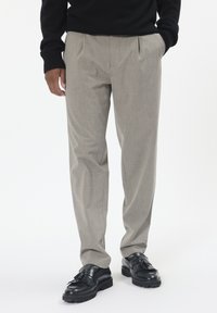 Gai pelēki plisēta bikses mīkstā audumā, ar taisnu kāju dizainu. Apvienotas ar melniem ādas mokasīniem.