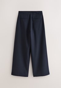 Tamsiai mėlynos plačios kelnių kojų kaprės, pagamintos iš tekstūruotos medžiagos, su paslėptu priekiu užsegimu, dviem užpakalinėmis kišenėmis ir neišdirbtais kraštais.