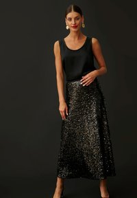 Top in satin nero abbinato a una lunga gonna nera con paillettes, caratterizzata da una texture scintillante e una vita aderente. L'outfit è completato da un paio di tacchi.