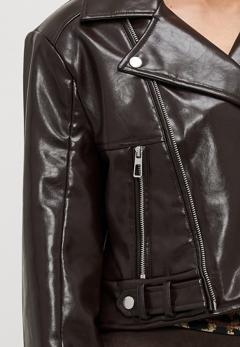 Veste de biker en simili cuir marron avec fermeture éclair asymétrique, détails à pression et silhouette ajustée. Caractéristiques : texture lisse et design court.