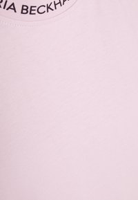 Svetle růžové tričko s kulatým výstřihem, na kterém je v tučném černém písmu napsáno "Victoria Beckham". Hladká, texturovaná tkanina.