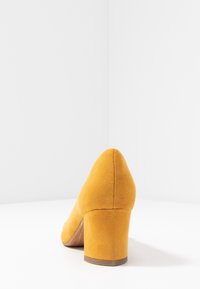 Scarpa con tacco alto in suede giallo, con punta arrotondata e tacco spesso. La texture è morbida, con una finitura liscia.