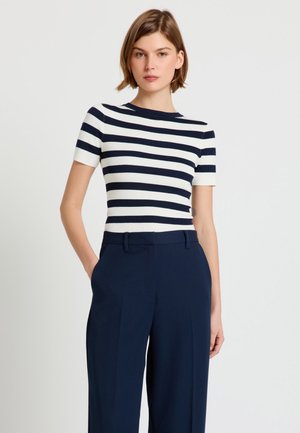 Woman wearing a navy and white horizontal striped short-sleeve top and navy high-waisted wide-leg trousers with hands in pockets.