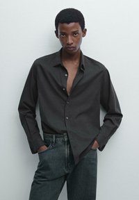 Donkergrijze blouse met lange mouwen, een spitse kraag en een knoopsluiting, gedragen met hooggerande, gestructureerde zwarte jeans. Eenvoudig ontwerp, geen patronen.