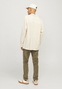 Cream-colored long-sleeve shirt with a loose fit, paired with olive green corduroy pants and white sneakers. Simple, textured fabric.