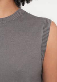 Pulover gri fără mâneci, cu textură nervurată și decolteu rotund, având o finisare curată la nivelul orificiilor pentru brațe și detalii subtile în țesătură.