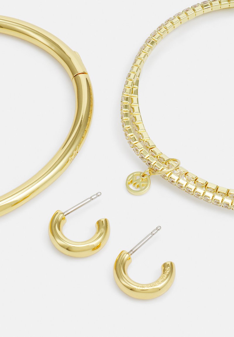 Goldfarbene Schmuckset bestehend aus einem glatten, geschwungenen Armreifen, einem strukturierten Choker mit klaren Steinen und Creolen mit glänzender Oberfläche.