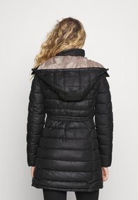 Černý péřový kabát se stáhnutým pasem, s hladkým béžovým panelem na ramenech a kapucí. Texturovaný, prošívaný design.